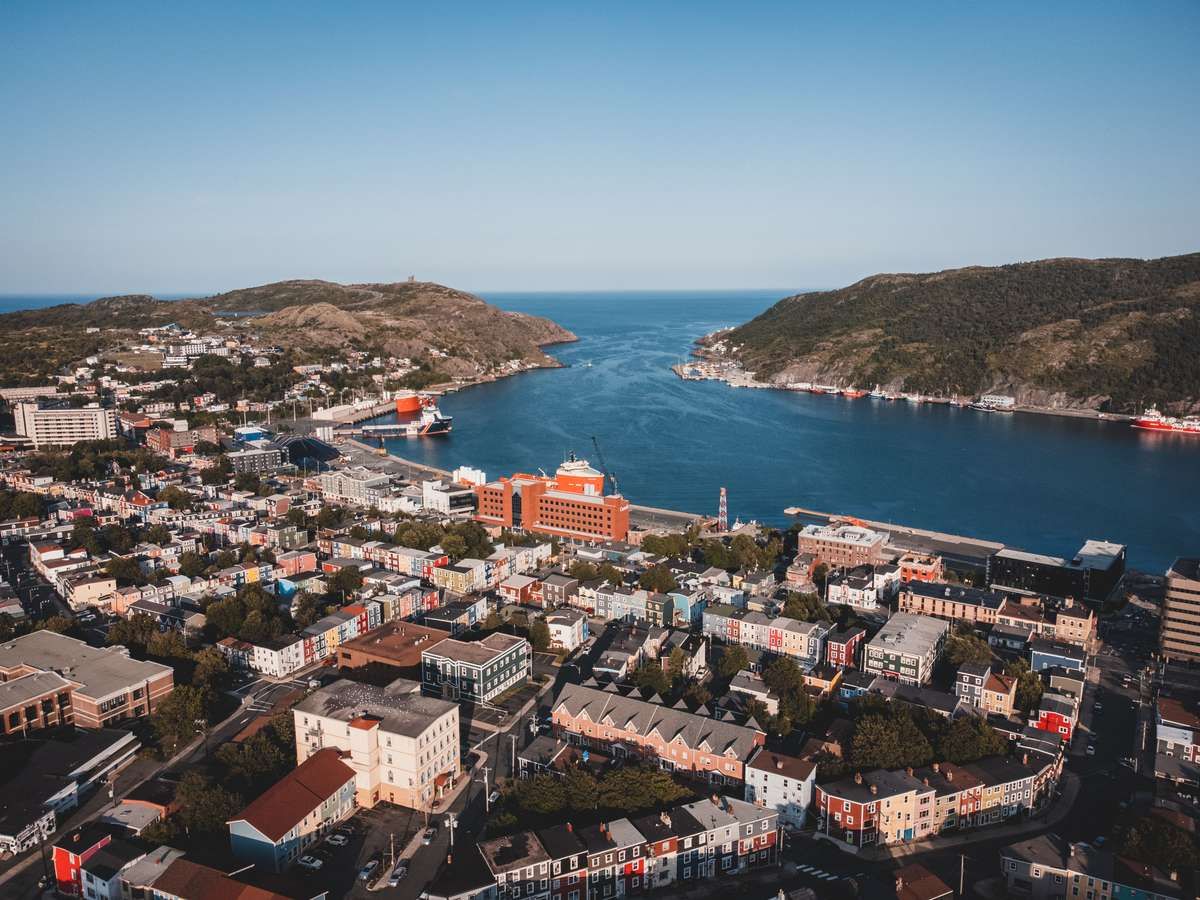 Aerial view of colorful houses and a harbor in St. John's, Newfoundland, surrounded by coastal hills.