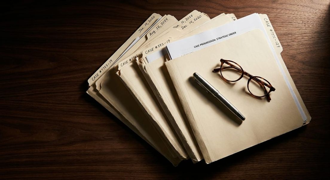 Photograph of manila legal case files, a silver pen, and glasses on a dark wood desk for a refugee appeal process.