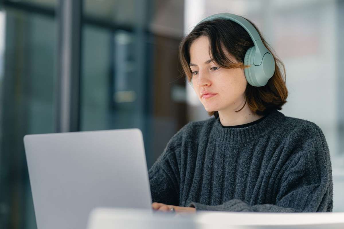 Woman wearing headphones works on a laptop at a desk.