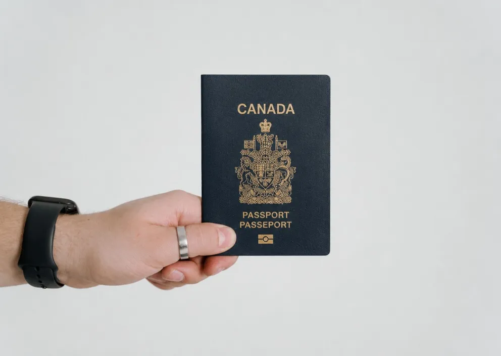 A hand holding a dark blue Canadian passport against a plain light background.