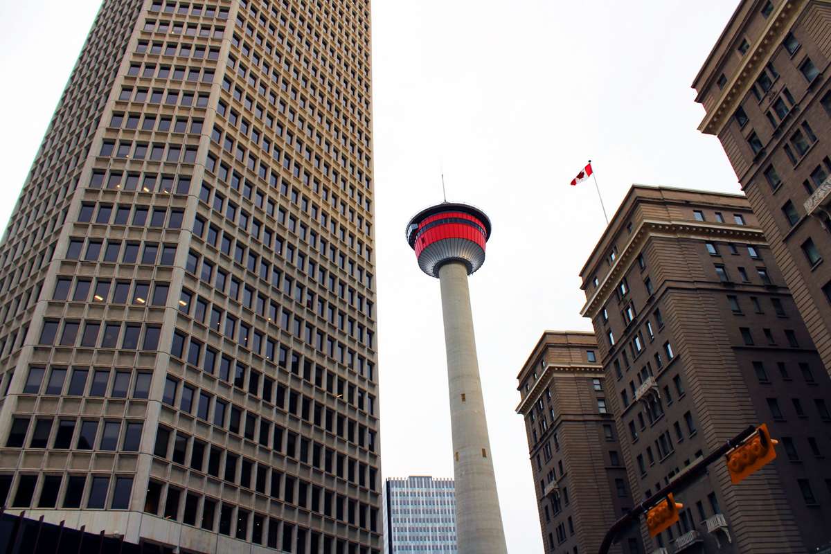 Low-angle view of the Calgary Tower framed by tall downtown skyscrapers.