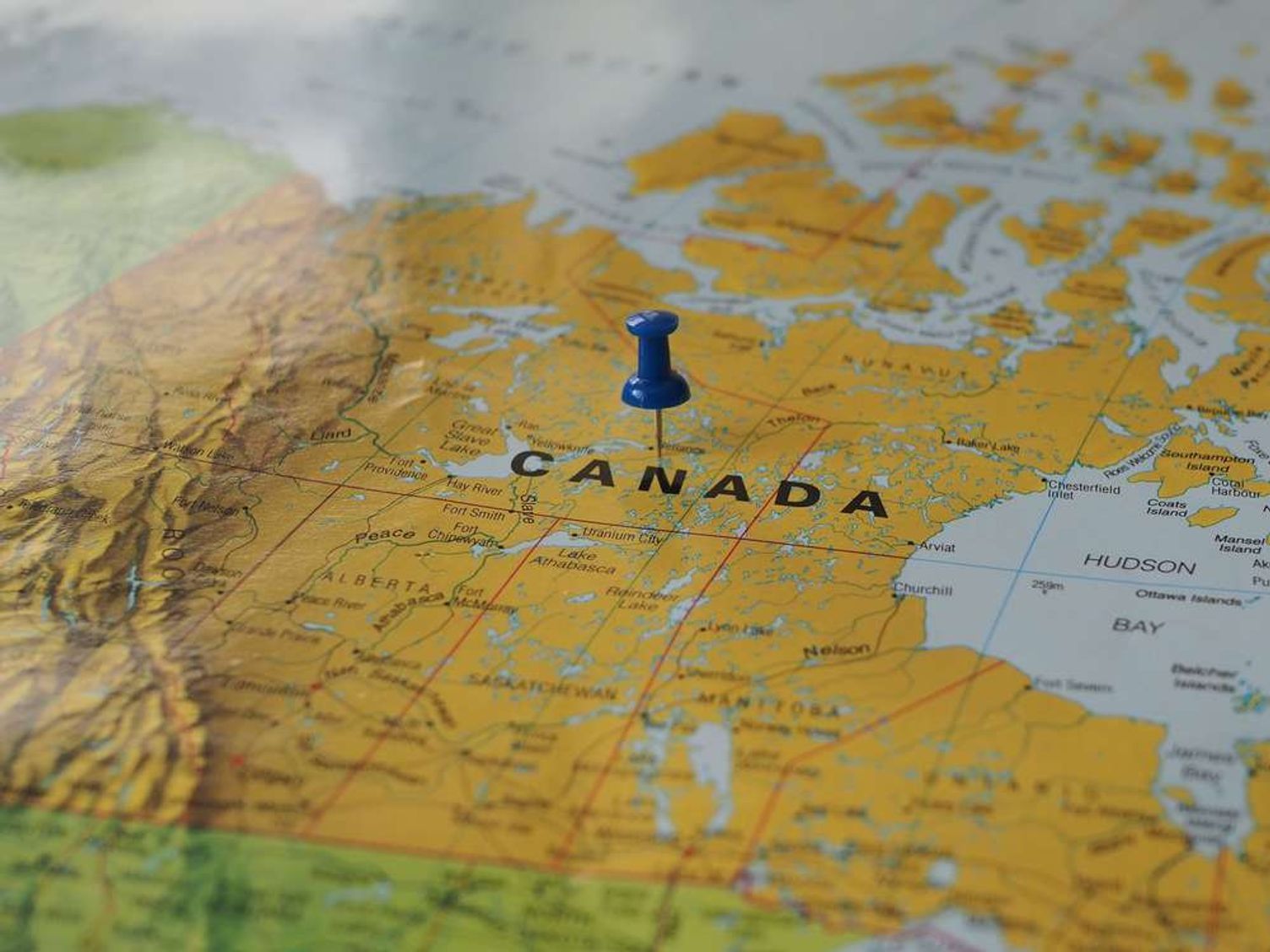 Close-up of a blue pushpin pinned on a map of Canada.