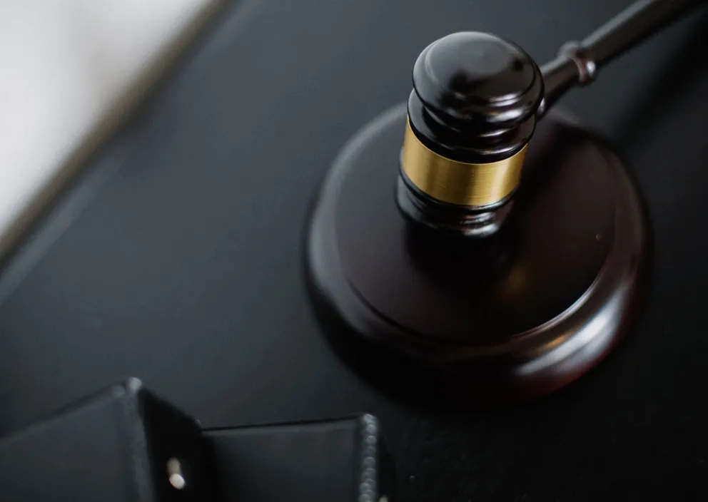 A wooden judge's gavel with a gold band resting on its sound block.