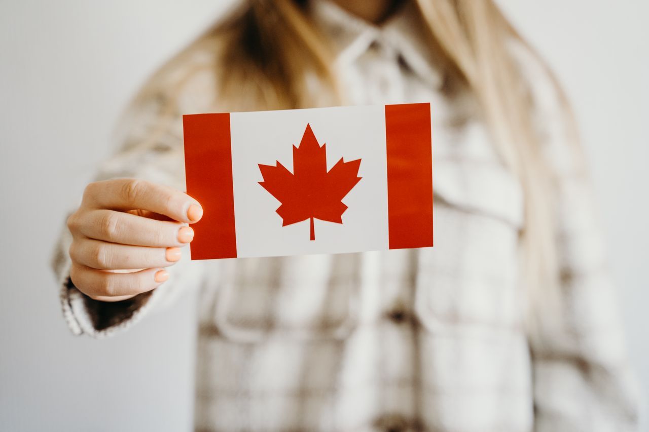 A person holding a small Canadian flag card in front of their chest.
