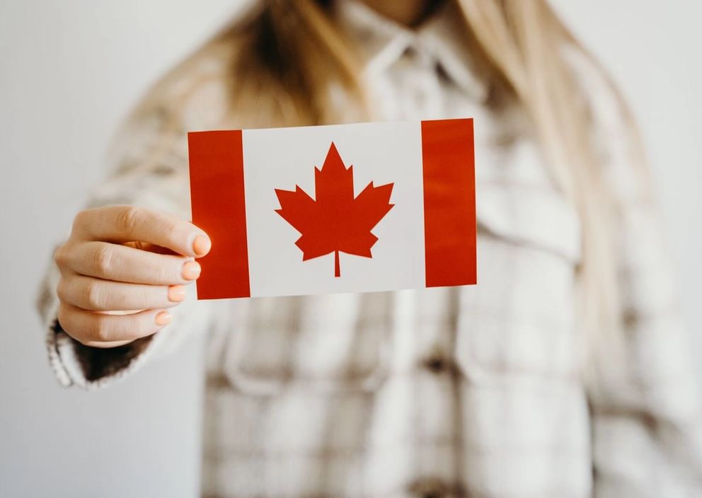 A person holding a small Canadian flag card in front of their chest.