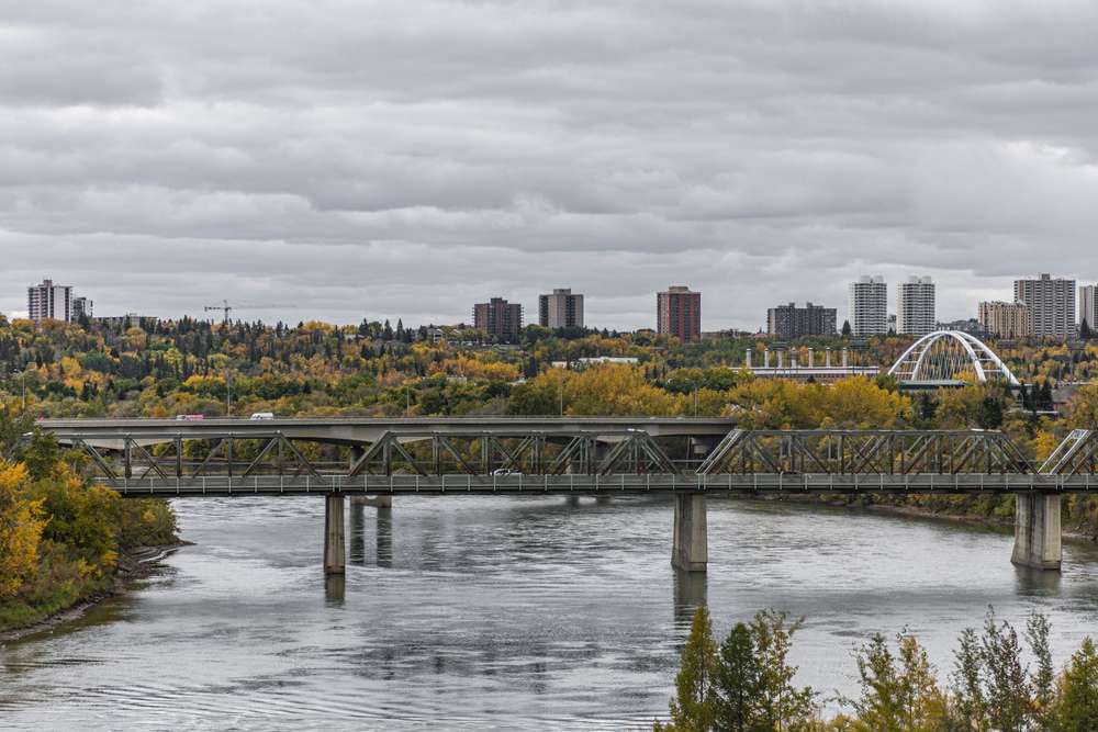 Bridges over the South Saskatchewan River in Saskatoon, showing the city skyline and yellow autumn trees.