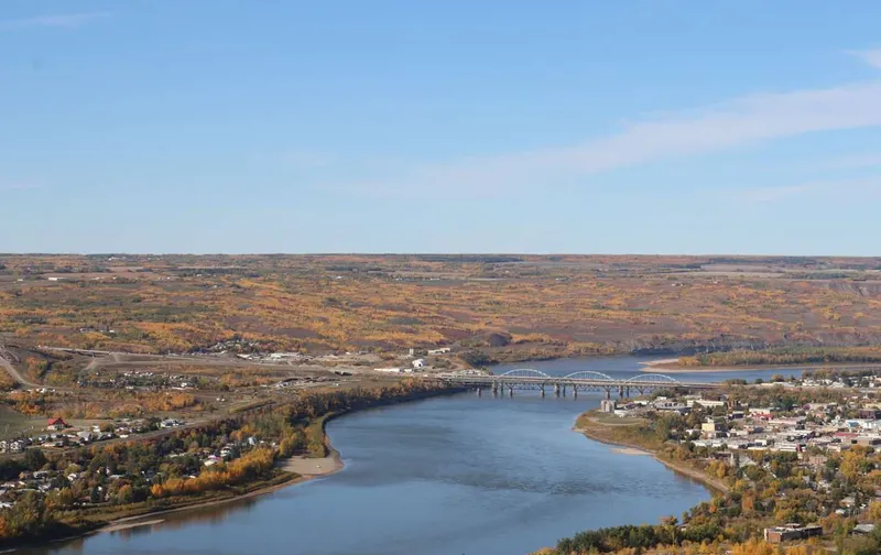 Aerial view of a wide river winding through a small town surrounded by colorful autumn foliage.