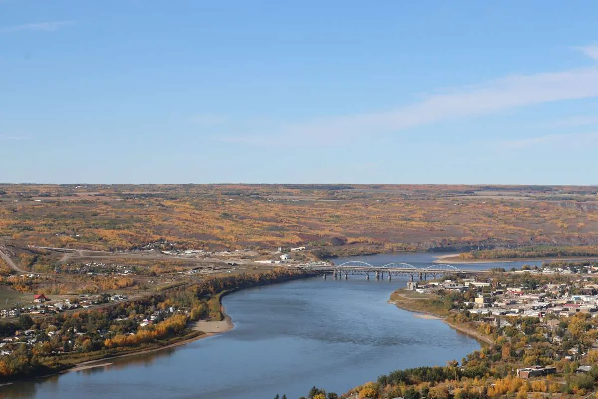 Aerial view of a wide river winding through a small town surrounded by colorful autumn foliage.