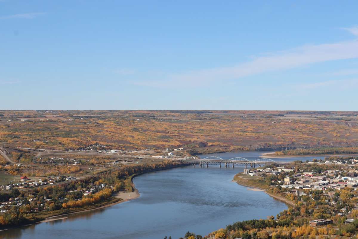 Aerial view of a wide river winding through a small town surrounded by colorful autumn foliage.