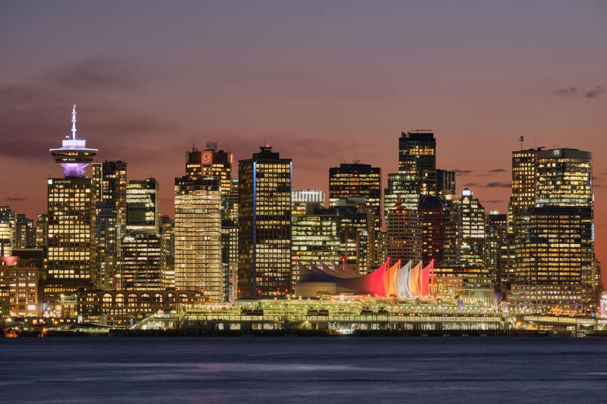 The illuminated downtown Vancouver skyline at dusk, featuring Canada Place along the waterfront.