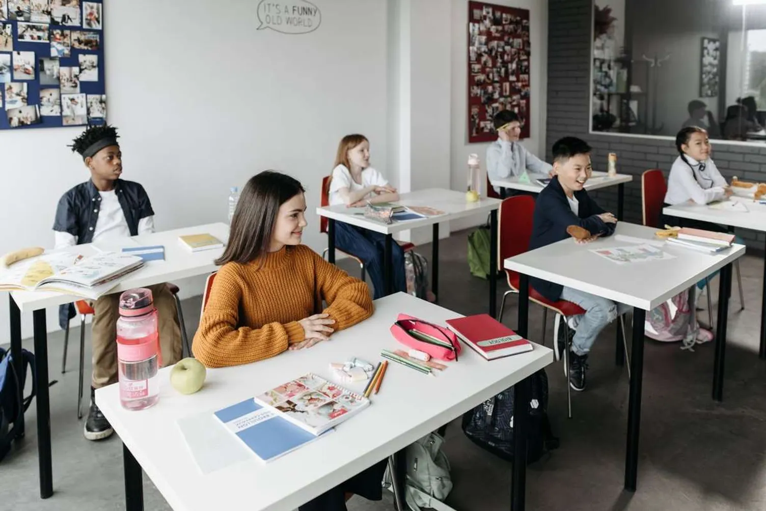 Diverse students sitting at desks with school supplies in a bright classroom.