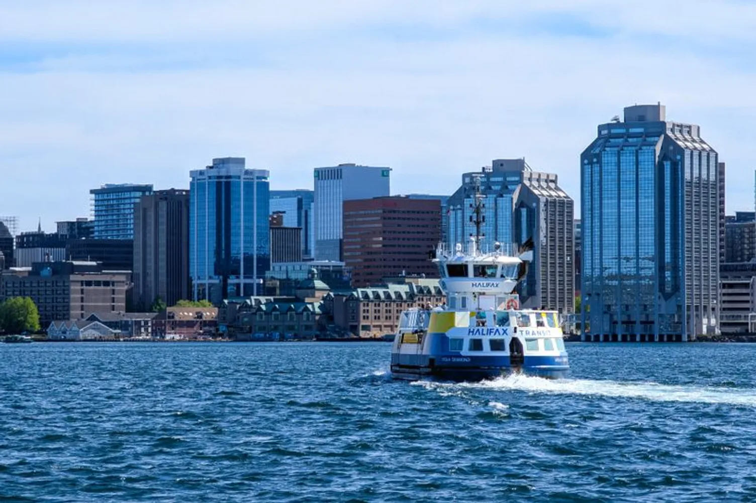A Halifax Transit ferry crosses the water with the downtown Halifax skyline in the background.