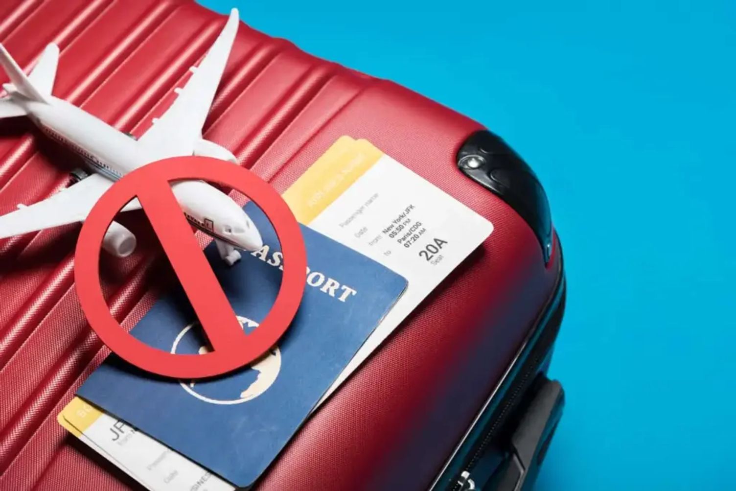 Travel ban concept with red suitcase, passport, boarding pass, toy airplane, and prohibition symbol