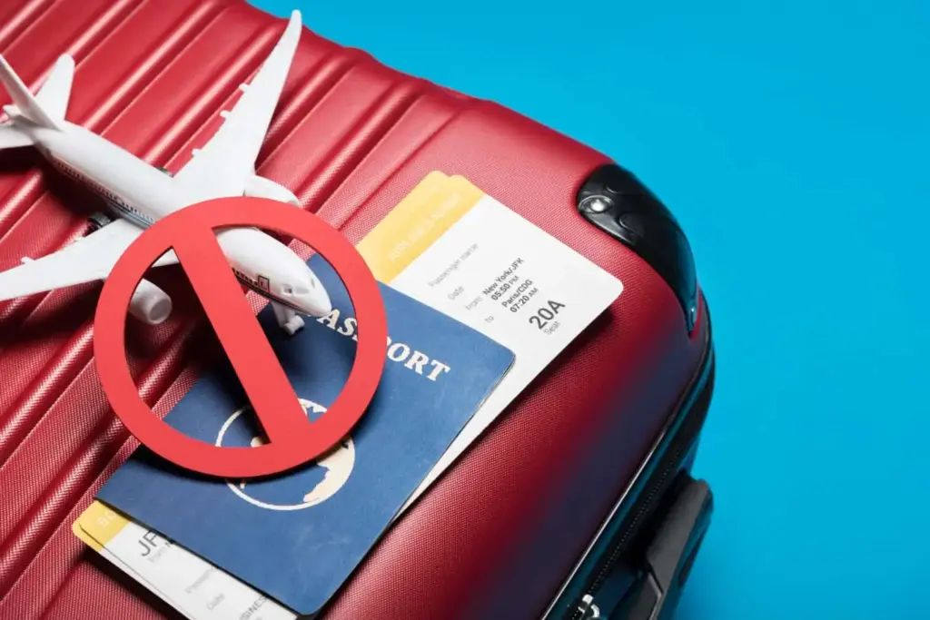 Travel ban concept with red suitcase, passport, boarding pass, toy airplane, and prohibition symbol