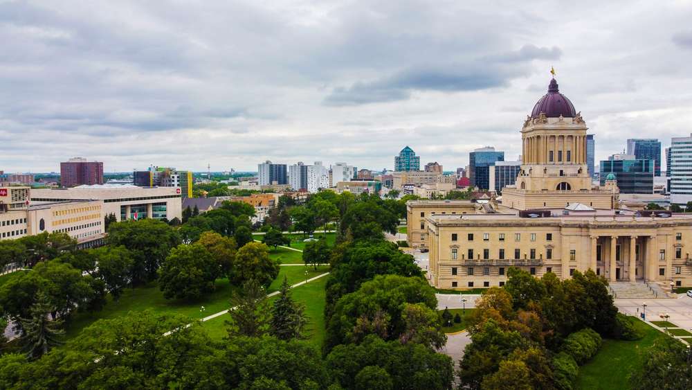 Aerial view of the Manitoba Legislative Building and surrounding park in Winnipeg under a cloudy sky.