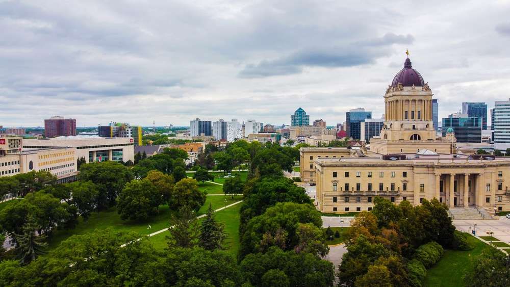 Aerial view of the Manitoba Legislative Building and surrounding park in Winnipeg under a cloudy sky.