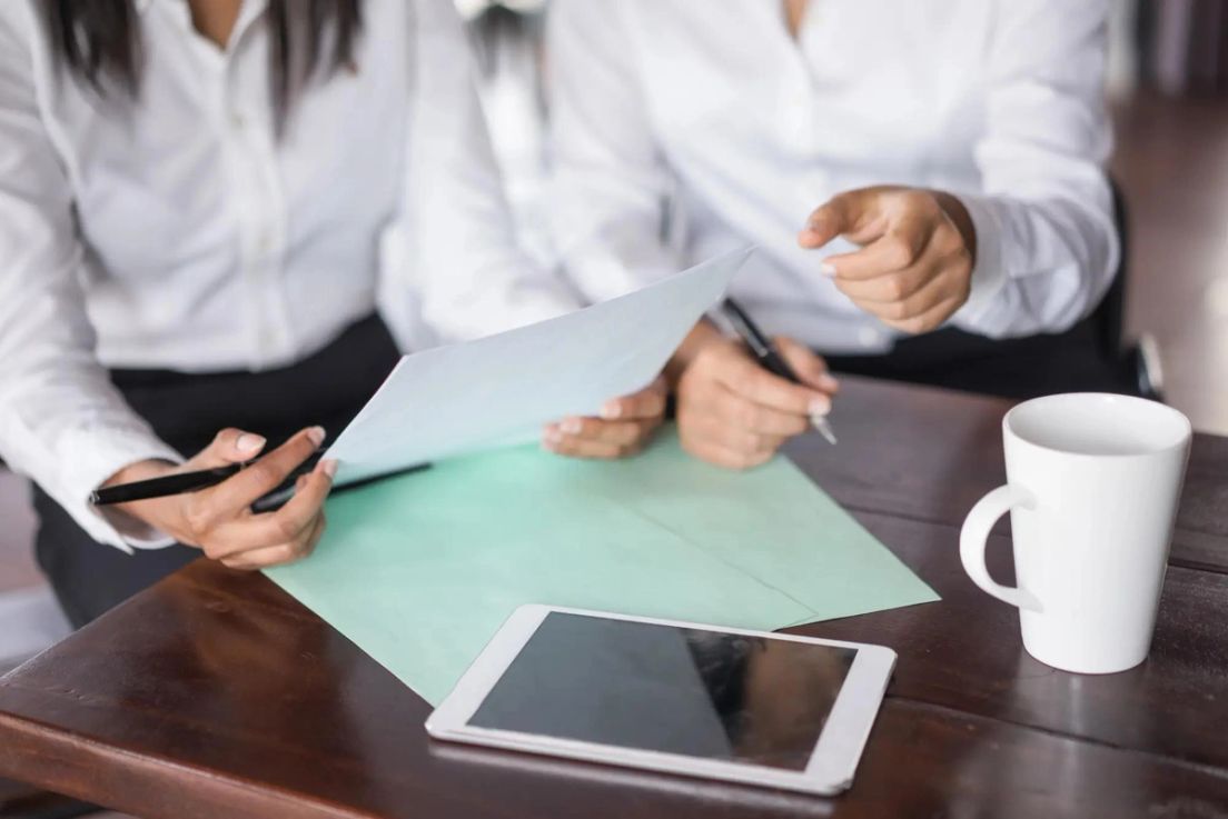 Two people reviewing documents with a tablet and coffee mug on the table, discussing permanent residence renewal.