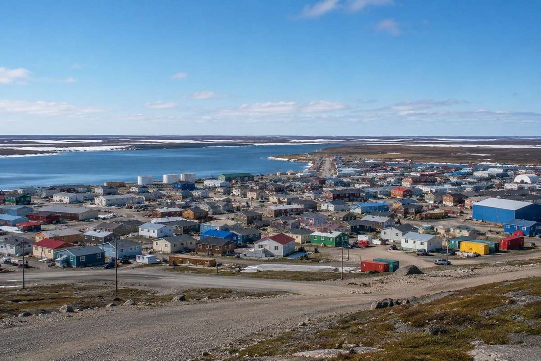 Elevated view of a remote northern town with colorful buildings along a body of water under a clear blue sky.