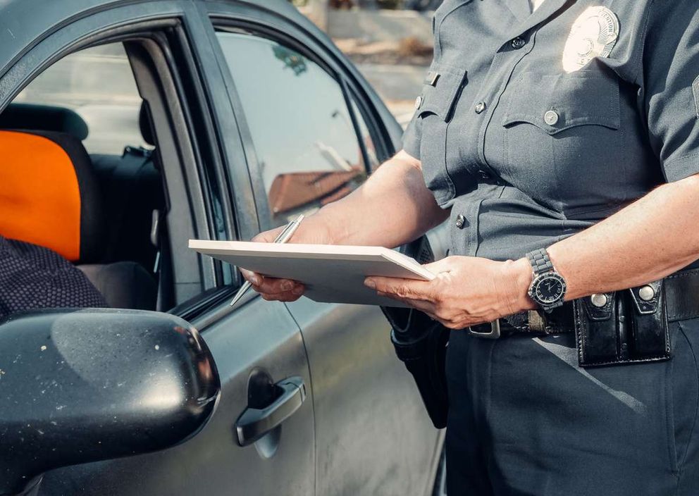 A police officer in uniform writing on a clipboard beside a car window.