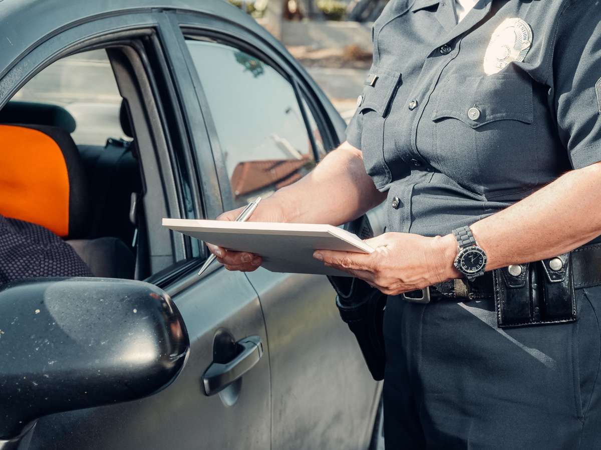 A police officer in uniform writing on a clipboard beside a car window.