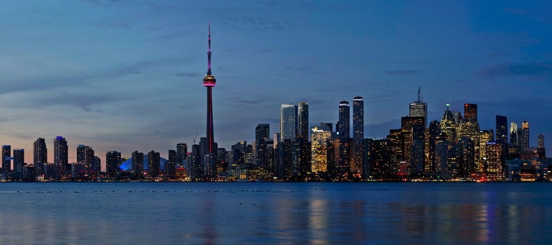 Toronto skyline with the illuminated CN Tower at dusk reflected in Lake Ontario.