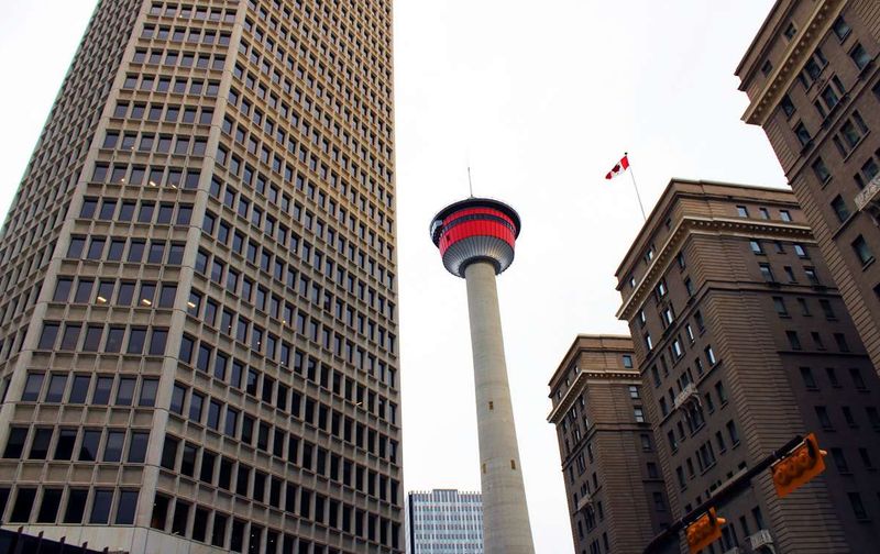 Low-angle view of the Calgary Tower framed by tall downtown skyscrapers.