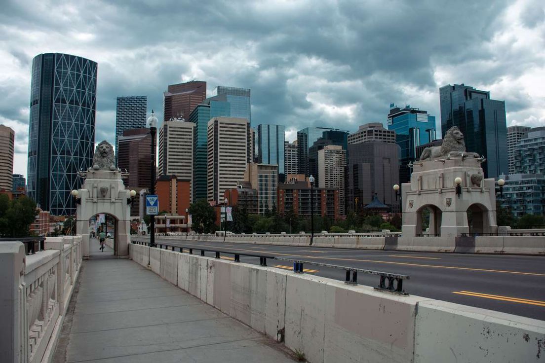 Downtown Calgary skyline viewed from the Centre Street Bridge with stone lion statues under cloudy skies.