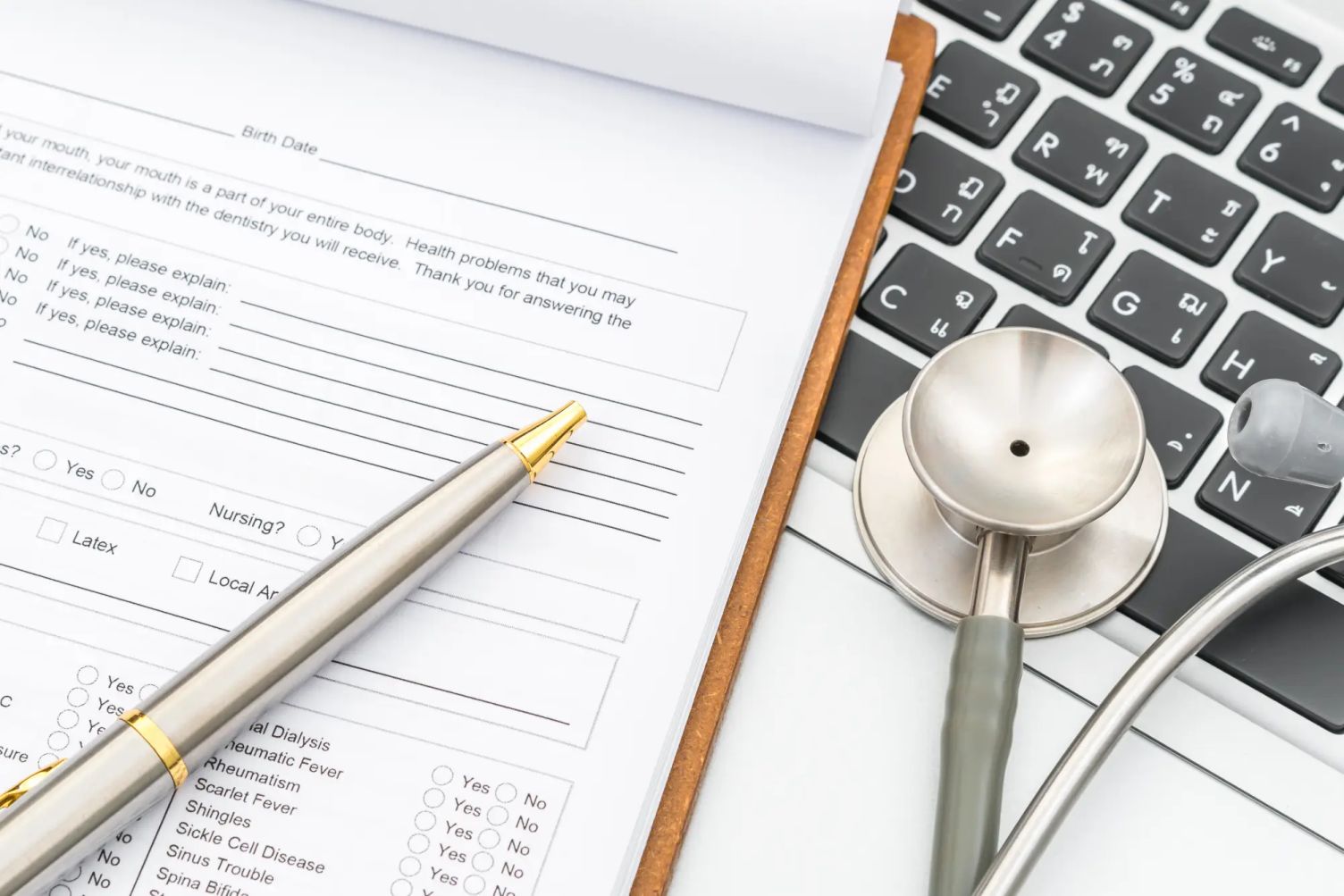Close-up of a medical form with a pen and stethoscope placed on a laptop keyboard, representing the concept of medical inadmissibility.