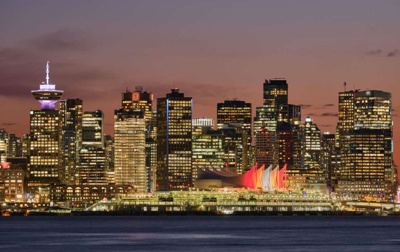 The illuminated downtown Vancouver skyline at dusk, featuring Canada Place along the waterfront.