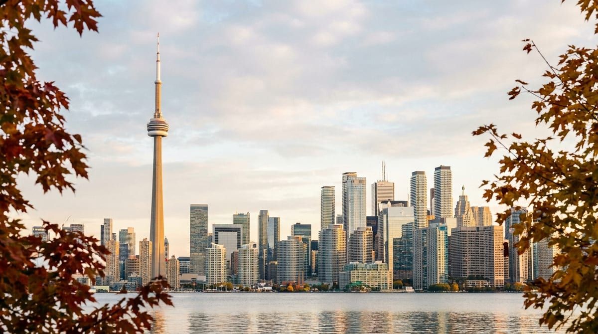 Panoramic golden hour view of the Toronto skyline and waterfront framed by subtle autumn foliage.