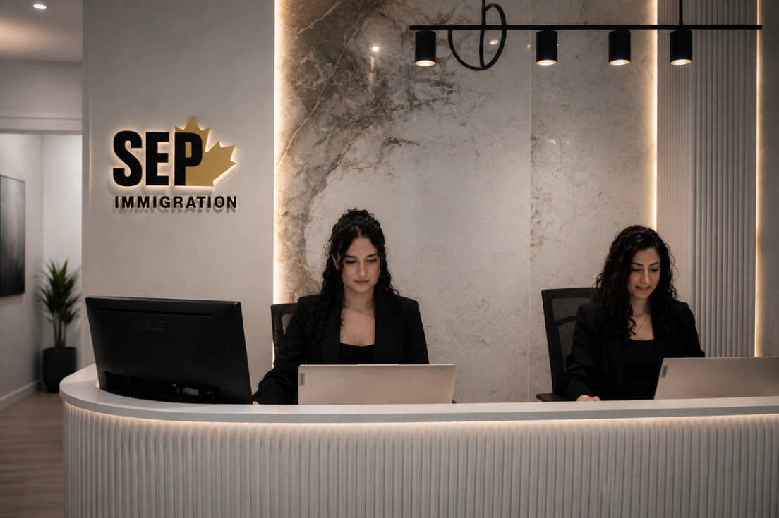 Two women working on laptops behind a white reception desk under a backlit SEP Immigration logo.