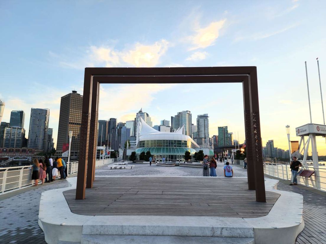 A large wooden frame on a Vancouver waterfront boardwalk framing Canada Place and downtown skyscrapers.