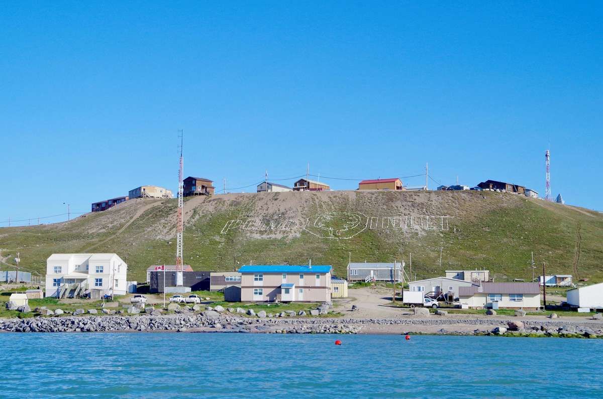 Coastal buildings in Pond Inlet, Nunavut, with the town's name spelled on a hill behind them.