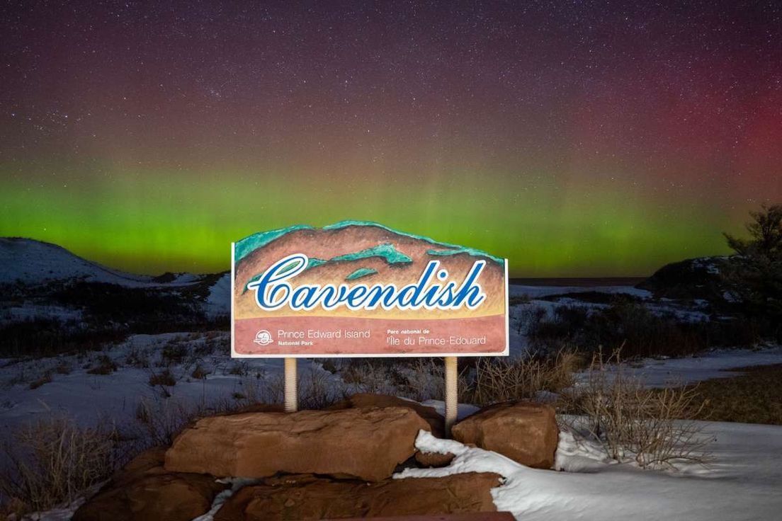 A sign for Cavendish in Prince Edward Island National Park under green northern lights at night.