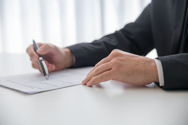 Close-up of a person in a suit holding a pen over a document on a white table.