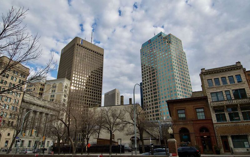 Tall office towers and historic buildings along a downtown street under a partly cloudy sky.