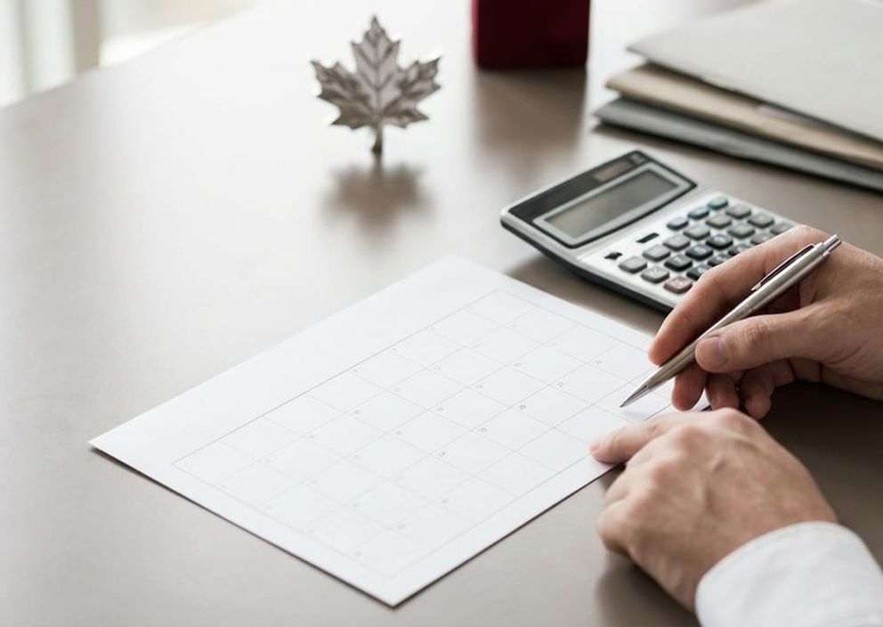 Hands using a calculator and calendar on a professional office desk, calculating Canadian citizenship eligibility days.