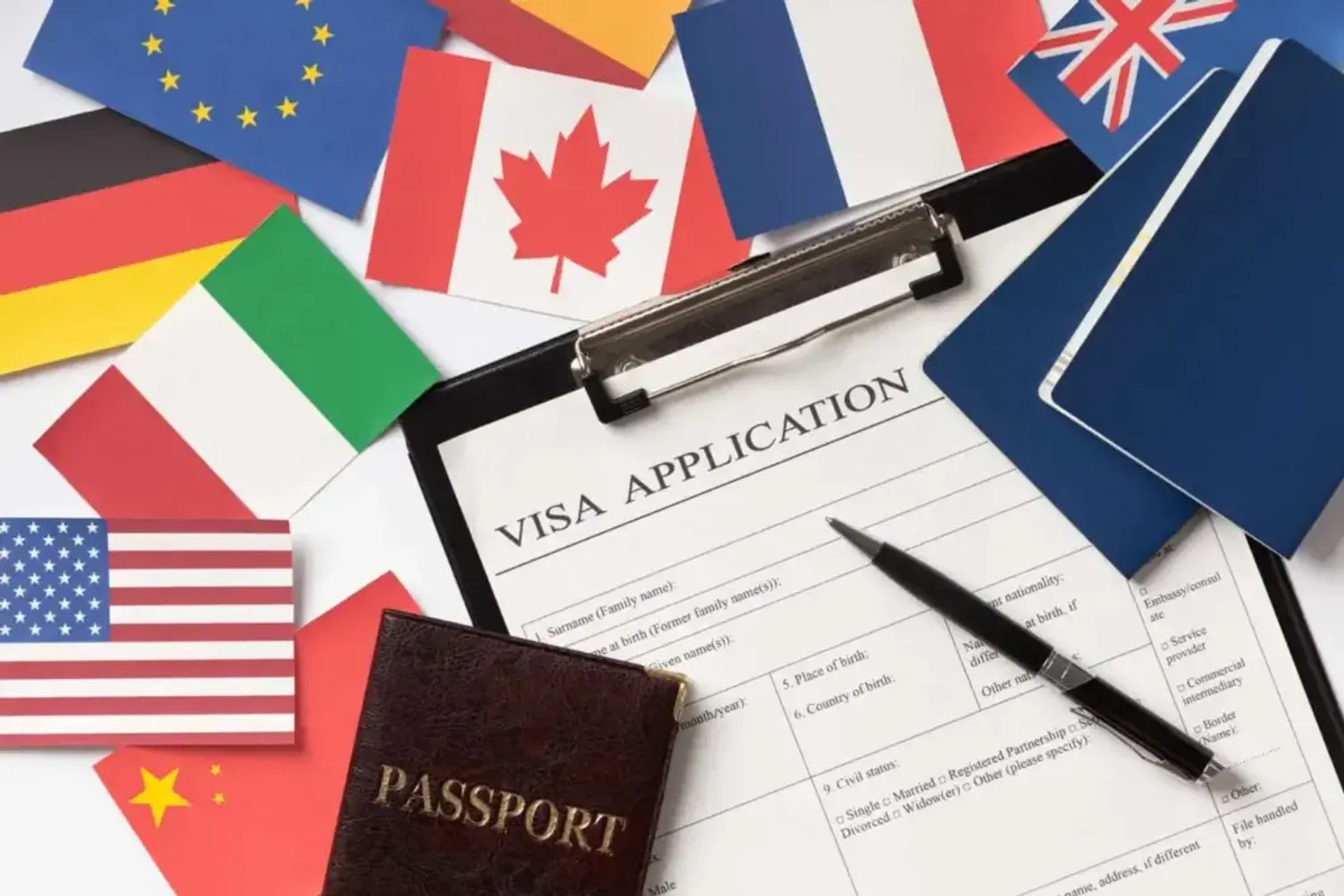 Visa application form with various national flags, passport, and pen on a desk
