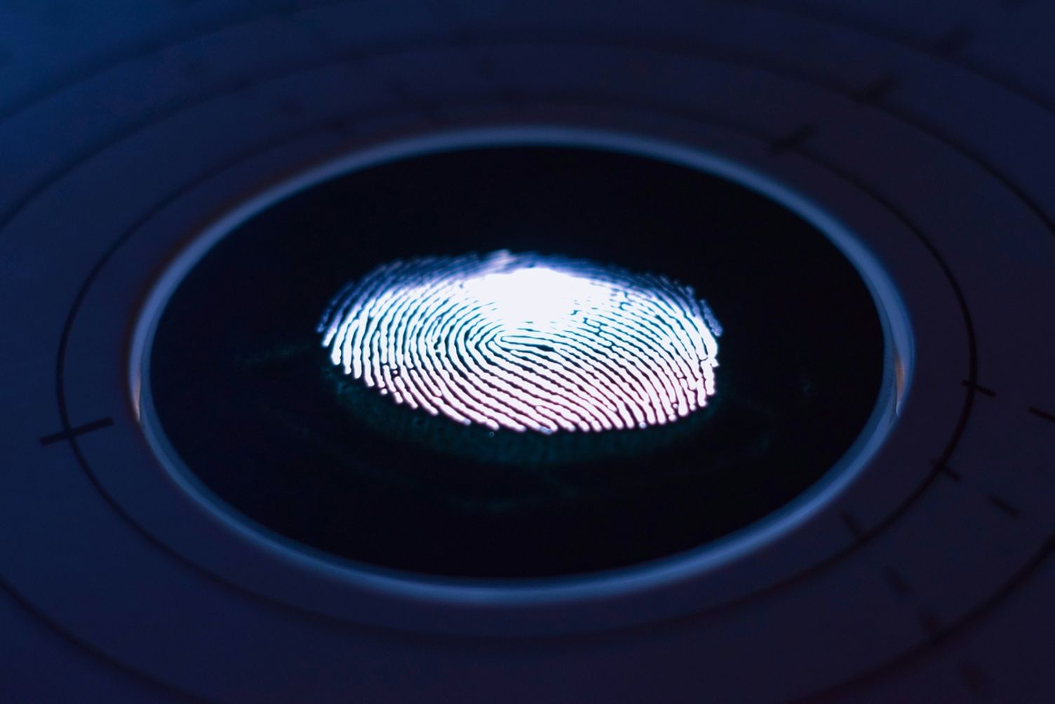 A glowing fingerprint scan illuminated on a dark circular biometric scanner.