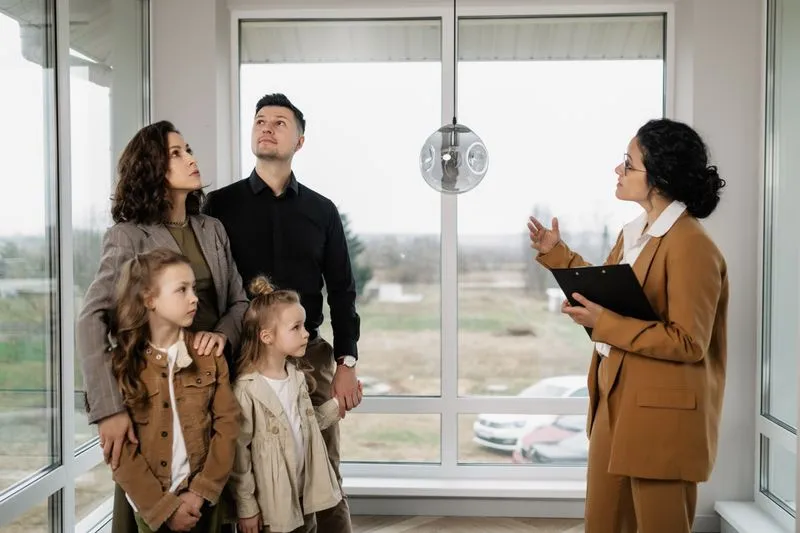 A real estate agent with a clipboard shows an apartment to a family of four.