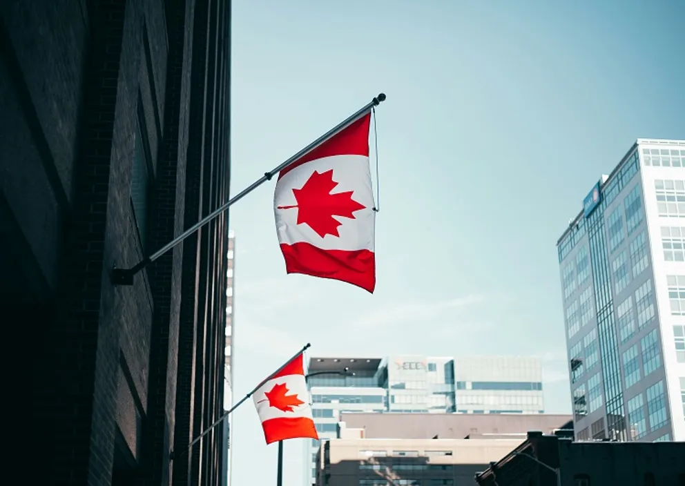 Canadian flags mounted on the exterior of an urban office building.