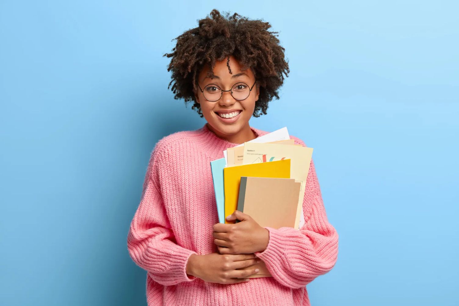Smiling student holding books and documents, representing changing Designated Learning Institution before arriving in Canada