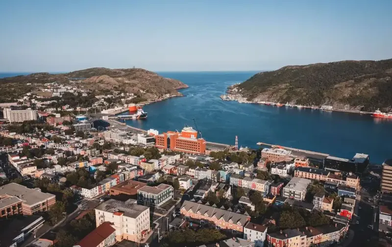 Aerial view of colorful houses and a harbor in St. John's, Newfoundland, surrounded by coastal hills.