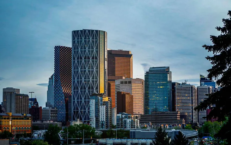 Modern downtown Calgary skyline featuring tall glass skyscrapers under a blue sky.