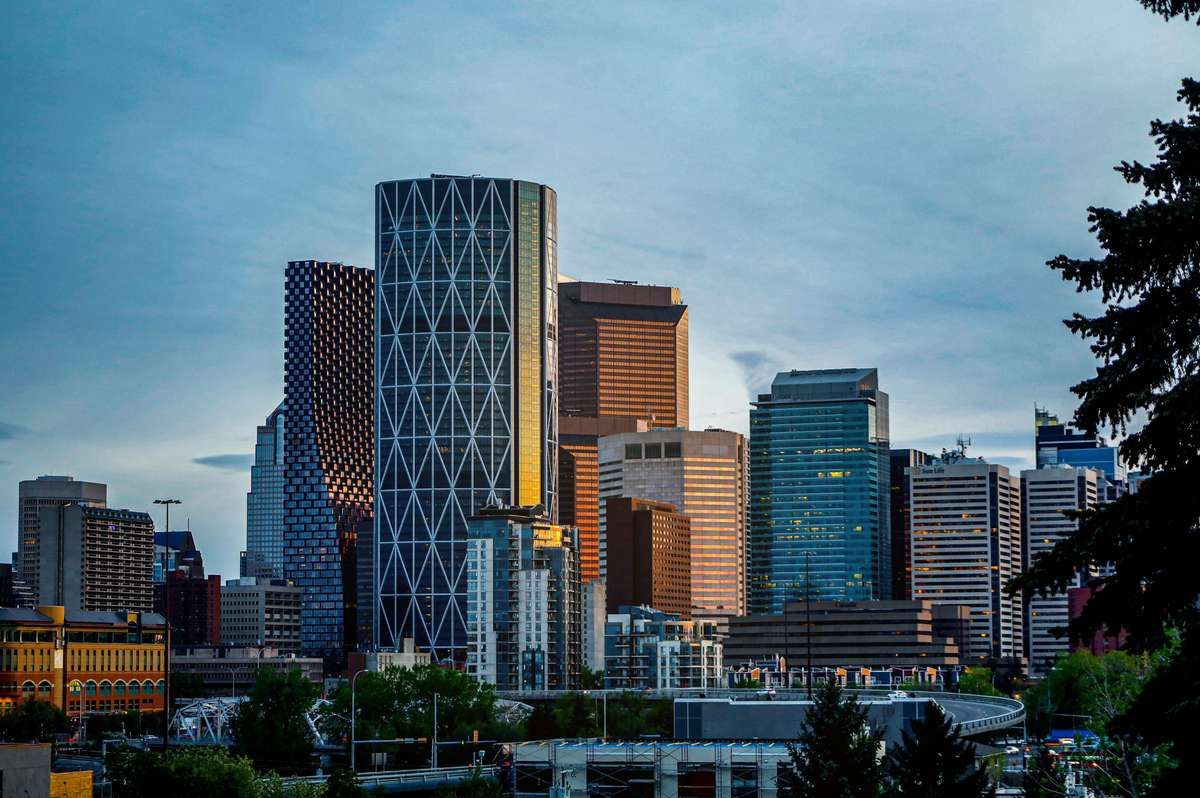 Modern downtown Calgary skyline featuring tall glass skyscrapers under a blue sky.