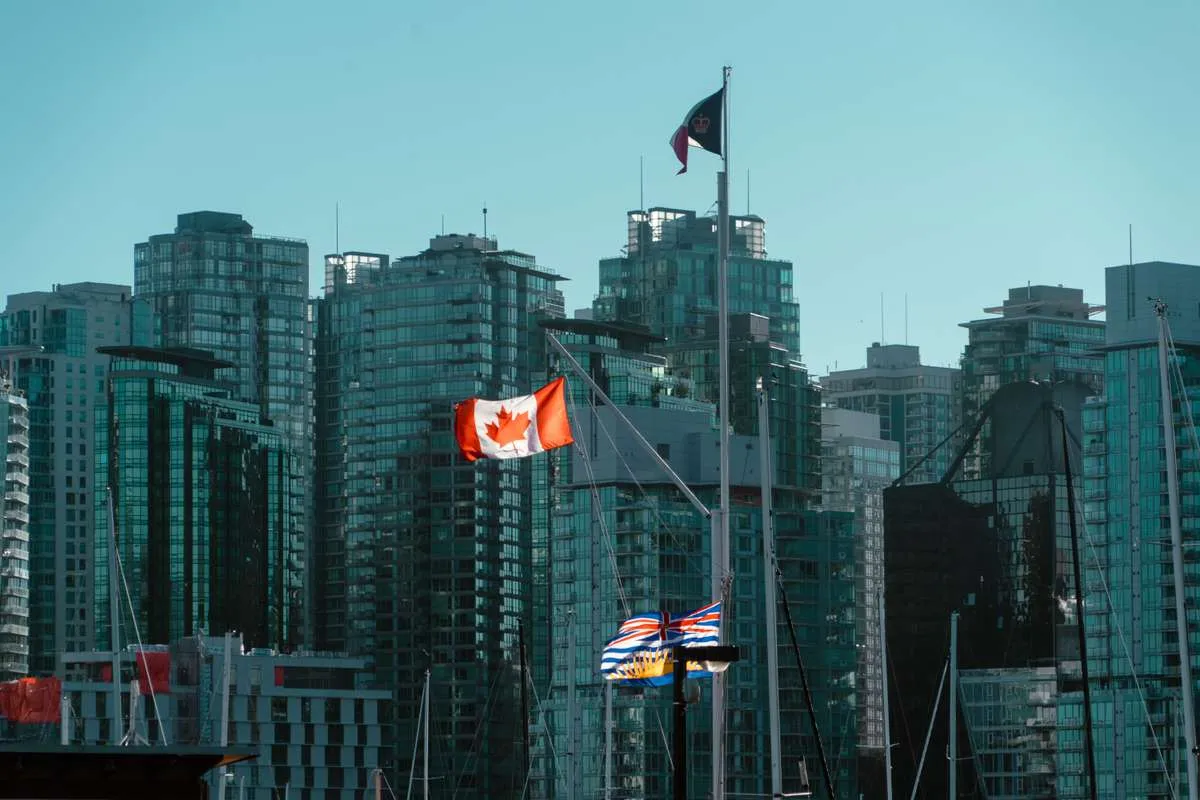 Canadian and British Columbia flags flying in front of modern glass high-rises in Vancouver.