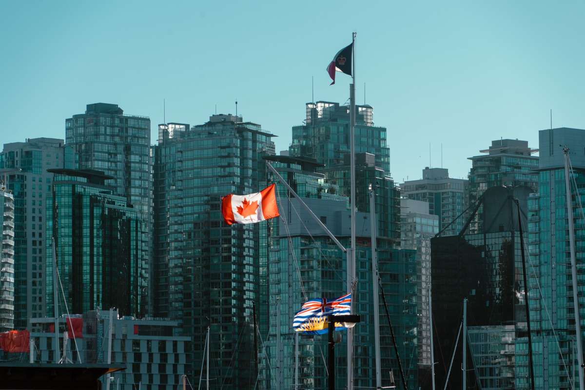 Canadian and British Columbia flags flying in front of modern glass high-rises in Vancouver.