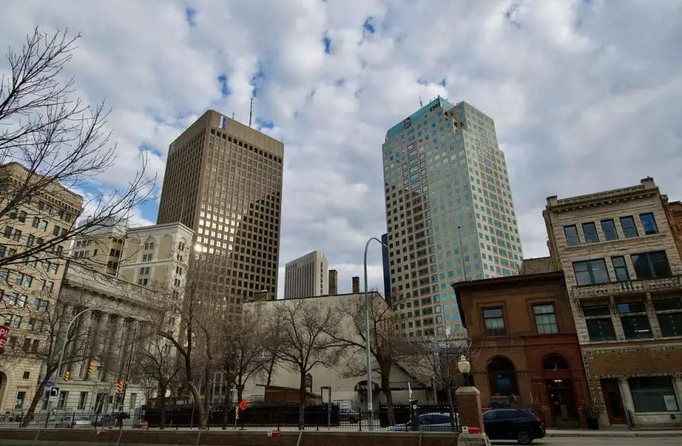 Tall office towers and historic buildings along a downtown street under a partly cloudy sky.