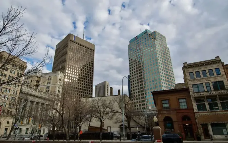 Tall office towers and historic buildings along a downtown street under a partly cloudy sky.