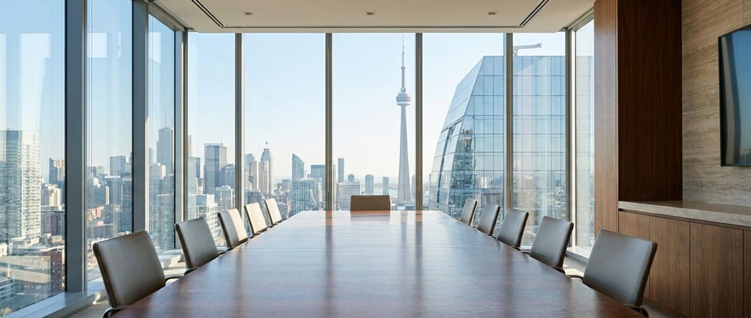 A bright, modern executive boardroom overlooking a clean Canadian city skyline through large glass windows.